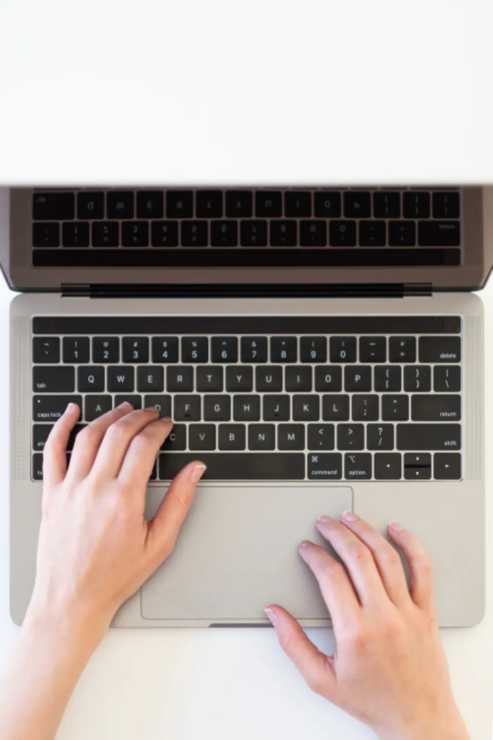 Overhead view of two hands resting on a laptop keyboard against a white desk, representing navigating a website without a mouse.
